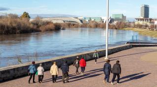 Varias personas pasean por la orilla del río Ebro a su paso por el recinto de la Expo de Zaragoza.