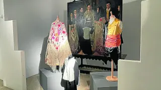 Tres trajes típicos fragatinos expuestos con ‘La boda fragatina’ de Miguel Viladrich de fondo.