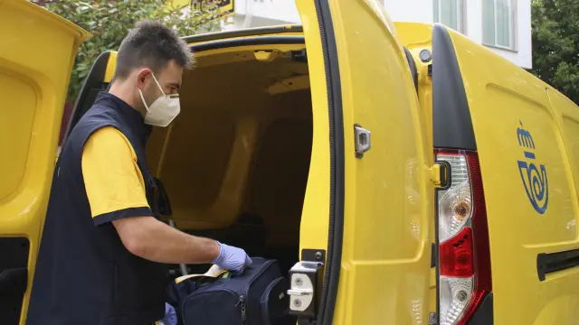 Un trabajador de la empresa de Correos introduce una maleta en una furgoneta de reparto.