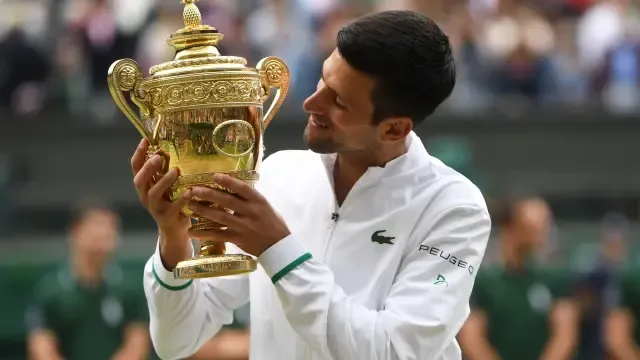 Djokovic mira al trofeo de campeón en la pista central de Wimbledon.
