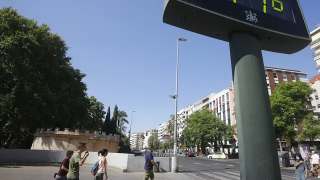 Unas personas caminan por una calle del centro de Córdoba junto a un termómetro que marca 41 grados