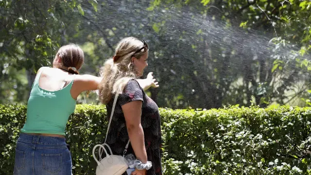 Dos jóvenes aprovechan el sistema de riego para refrescarse durante un paseo por Madrid.