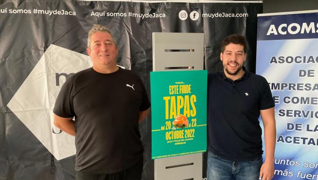 Fran Ponce y Alejandro Carbonell, junto al cartel del concurso, en la sede de Acomseja en Jaca.