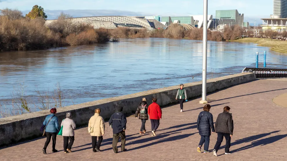 Varias personas pasean por la orilla del río Ebro a su paso por el recinto de la Expo de Zaragoza.