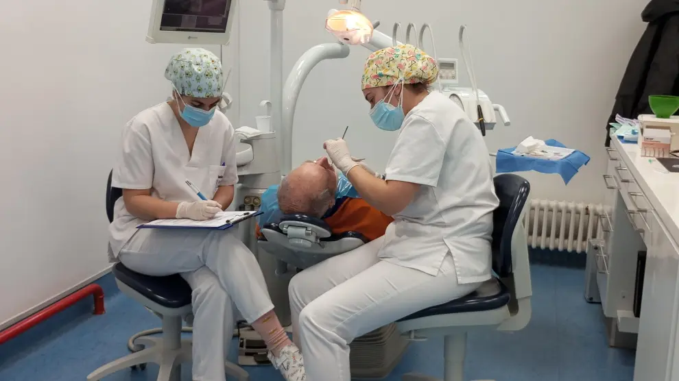 Dos alumnas de 5º curso de Odontología realizando prácticas en la clínica con un paciente.