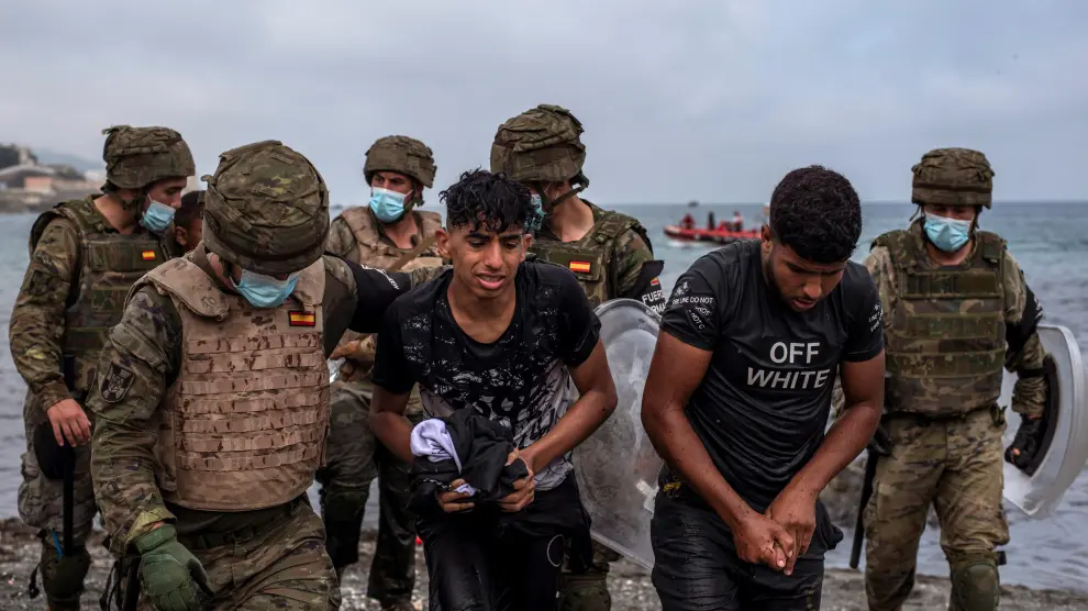 Soldados del Ejército ayudan a dos jóvenes a salir del agua en la playa de El Tarajal de Ceuta.