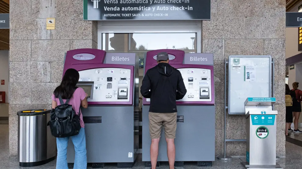 Dos personas sacan billetes en máquinas autoventa de una estación de Renfe.