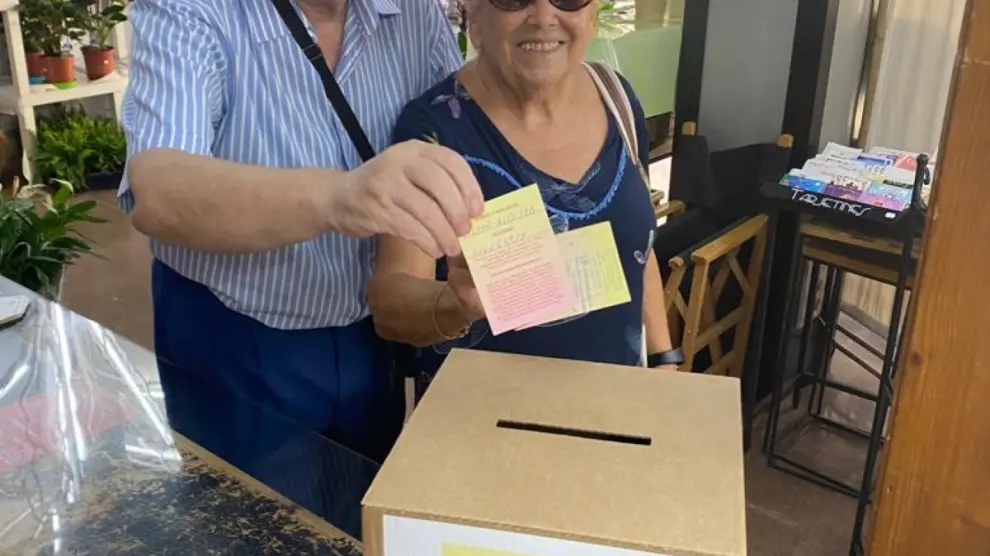 Dos usuarios echan papeletas selladas a la urna para el sorteo de El Monegrazo del verano.