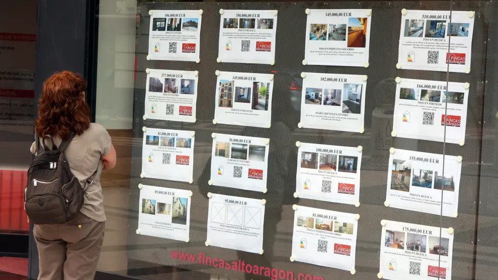 Una mujer, mirando anuncios de viviendas a la venta o en alquiler en una inmobiliaria de Huesca.