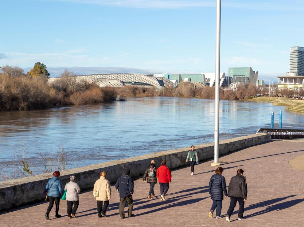 Varias personas pasean por la orilla del río Ebro a su paso por el recinto de la Expo de Zaragoza.