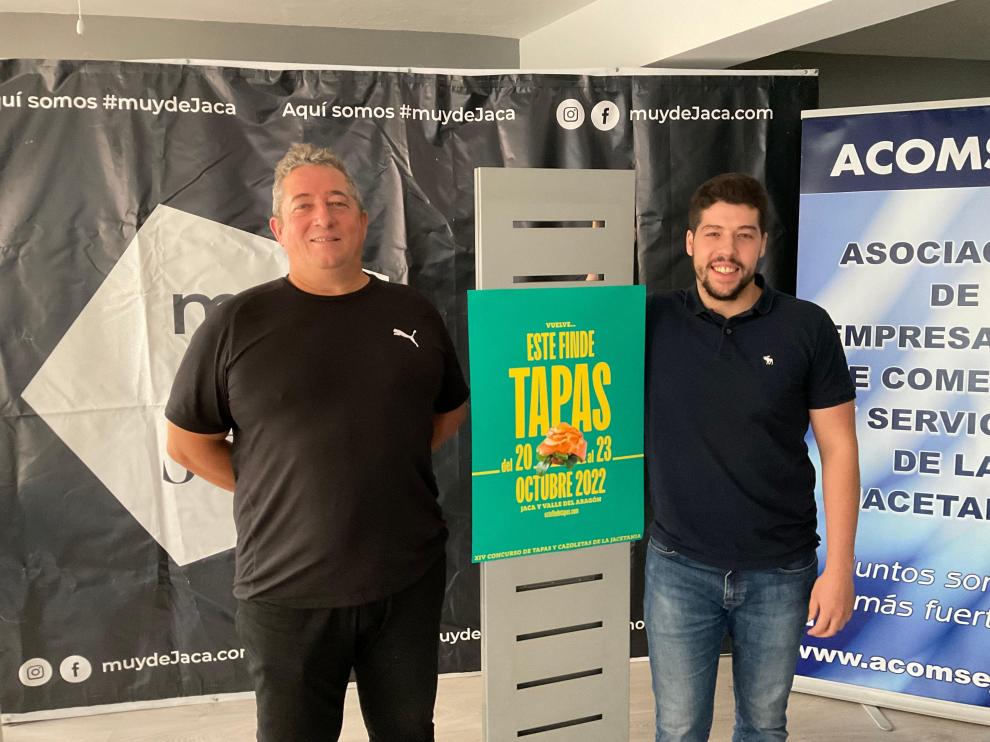 Fran Ponce y Alejandro Carbonell, junto al cartel del concurso, en la sede de Acomseja en Jaca.