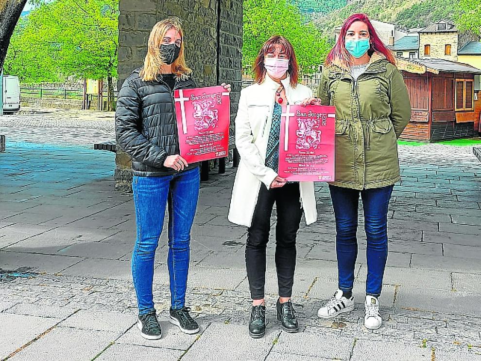 Andrea Gavín, Nuria Pargada y Marta Luis muestran el cartel de la programación de San Jorge en Biescas.