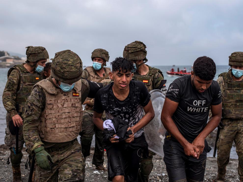 Soldados del Ejército ayudan a dos jóvenes a salir del agua en la playa de El Tarajal de Ceuta.