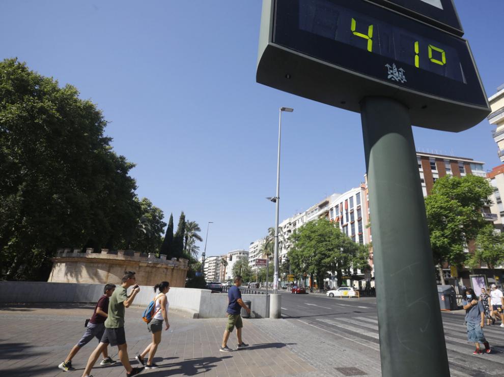 Unas personas caminan por una calle del centro de Córdoba junto a un termómetro que marca 41 grados