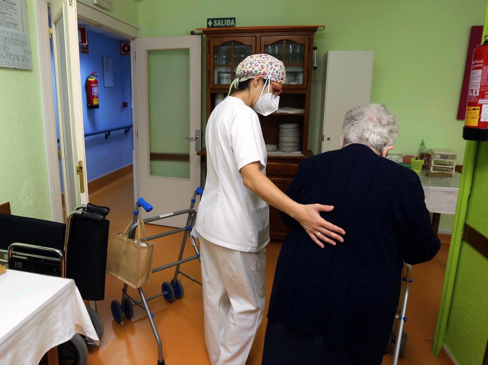 Trabajadora de la residencia Avenida, de Huesca, ayuda a una residente a desplazarse.