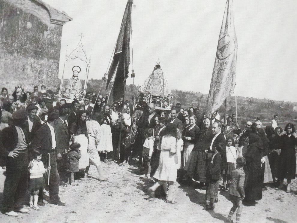 El pueblo de Sariñena, de todas las edades, asiste a la procesión del año 1934, con banderas y santos identificados en la imagen.