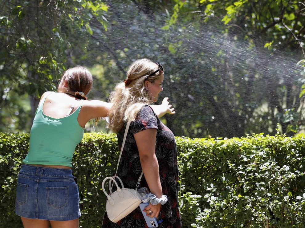 Dos jóvenes aprovechan el sistema de riego para refrescarse durante un paseo por Madrid.