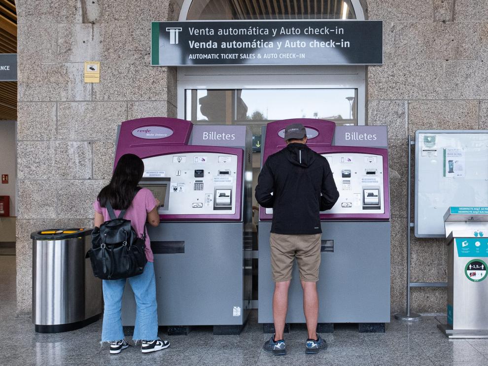 Dos personas sacan billetes en máquinas autoventa de una estación de Renfe.